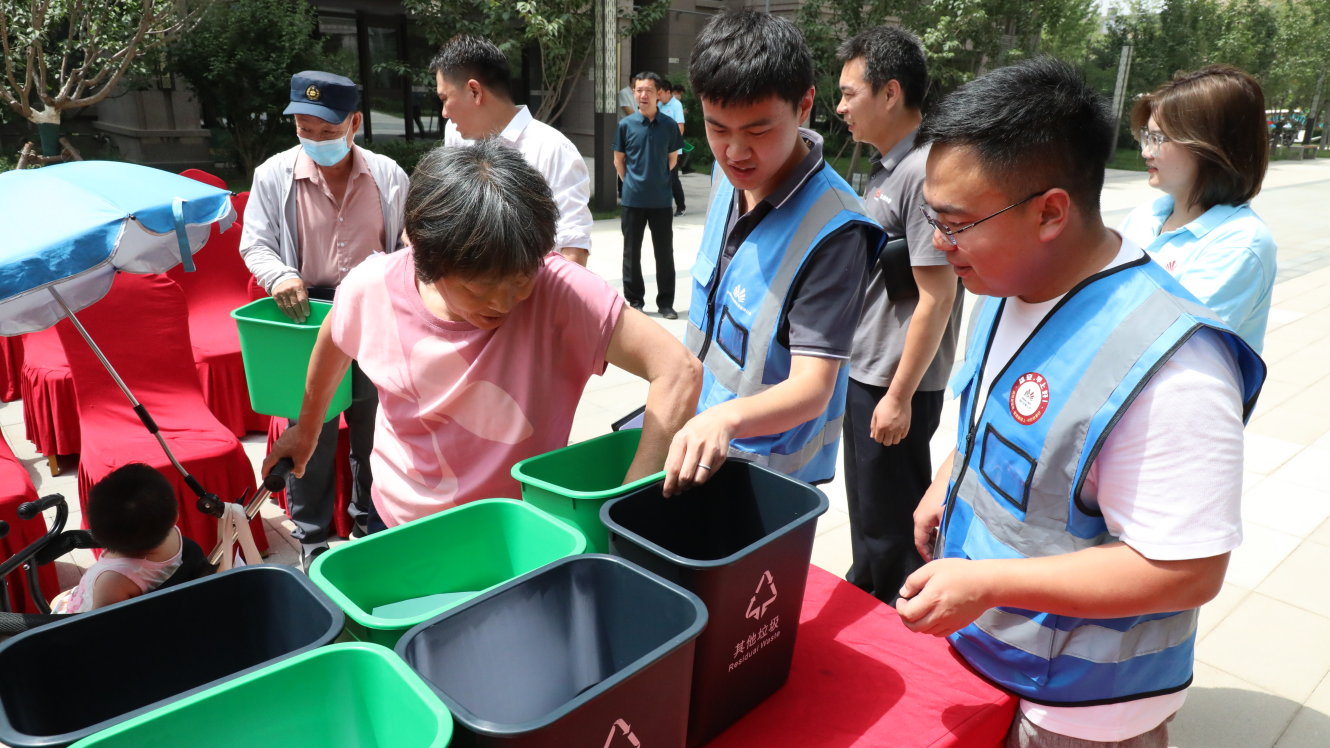 “垃圾分類志愿服務(wù)隊”隊員向居民發(fā)放垃圾桶。生態(tài)建設(shè)公司供圖